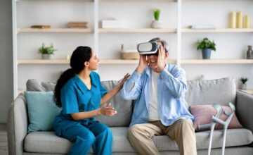 Elderly man using VR headset with young medical worker, exploring augmented reality at retirement home Elderly man using VR headset with young medical worker, exploring augmented reality at retirement home