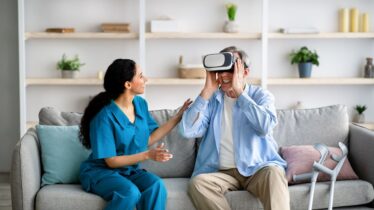 Elderly man using VR headset with young medical worker, exploring augmented reality at retirement home